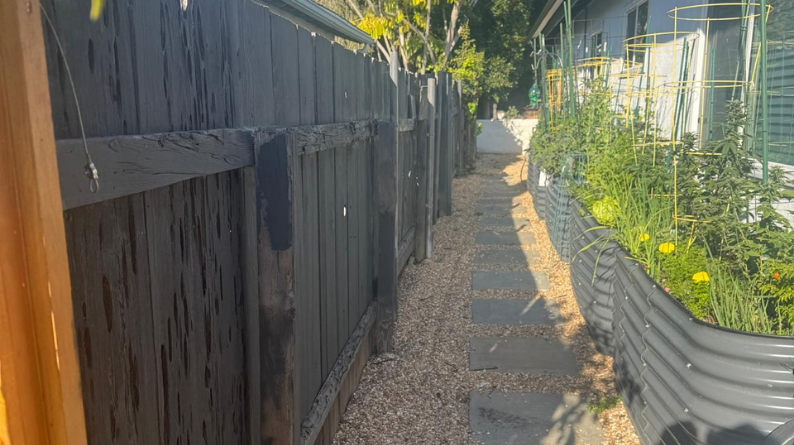 Weathered dark fence lining a side yard path with stepping stones