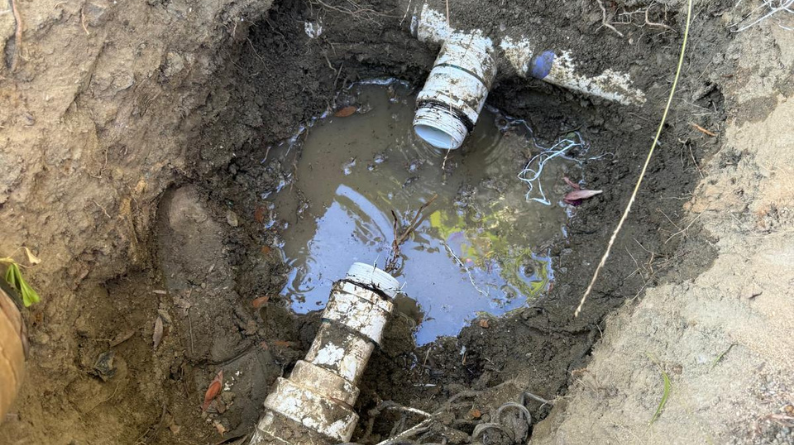 Broken PVC irrigation pipe leaking into a muddy hole
