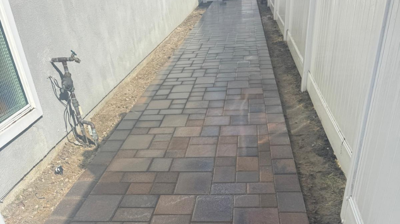 New paver walkway installed between a house wall and white fence