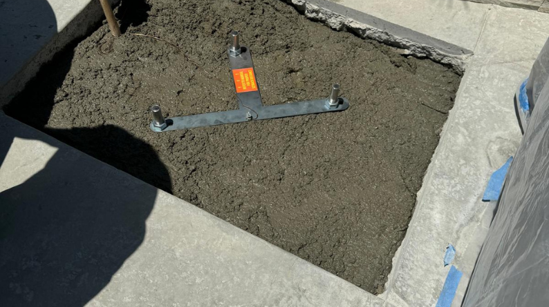 Fresh concrete footing poured in a square cutout with anchor bolts in place