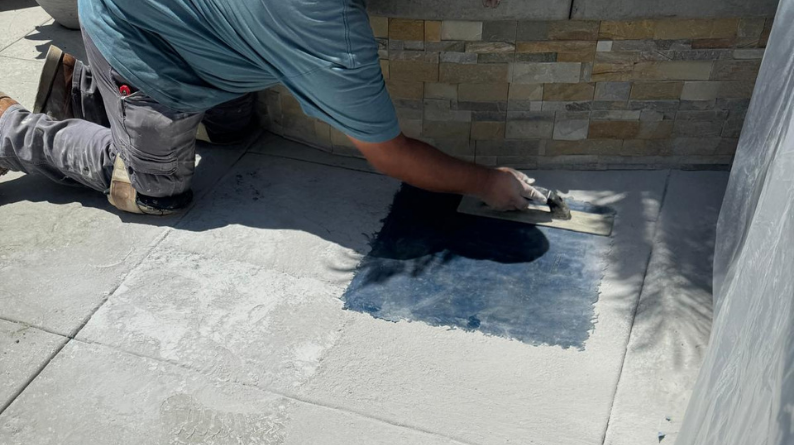 Contractor applying sealer to pavers with a hand trowel near a stone wall