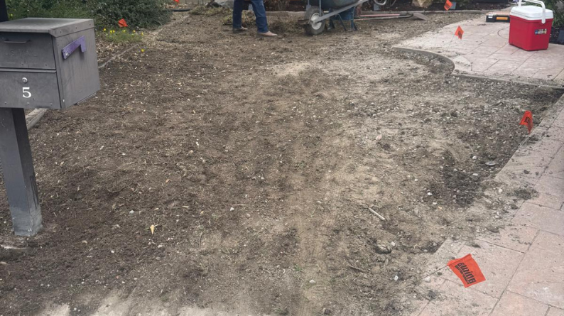 Front yard cleared to soil with utility flags and landscaping equipment
