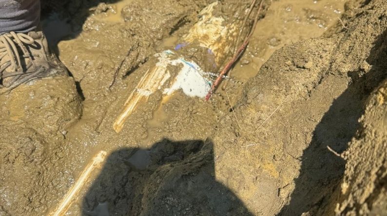 Broken sprinkler line uncovered in wet soil as repair work begins