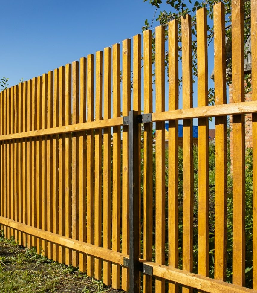 Close-up of a new wooden picket fence in the backyard of a country house, a sunny summer day.